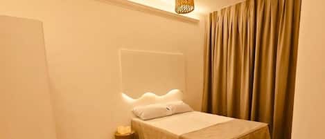 A bedroom with a bed, bedside tables, a hanging light fixture, and a curtain.