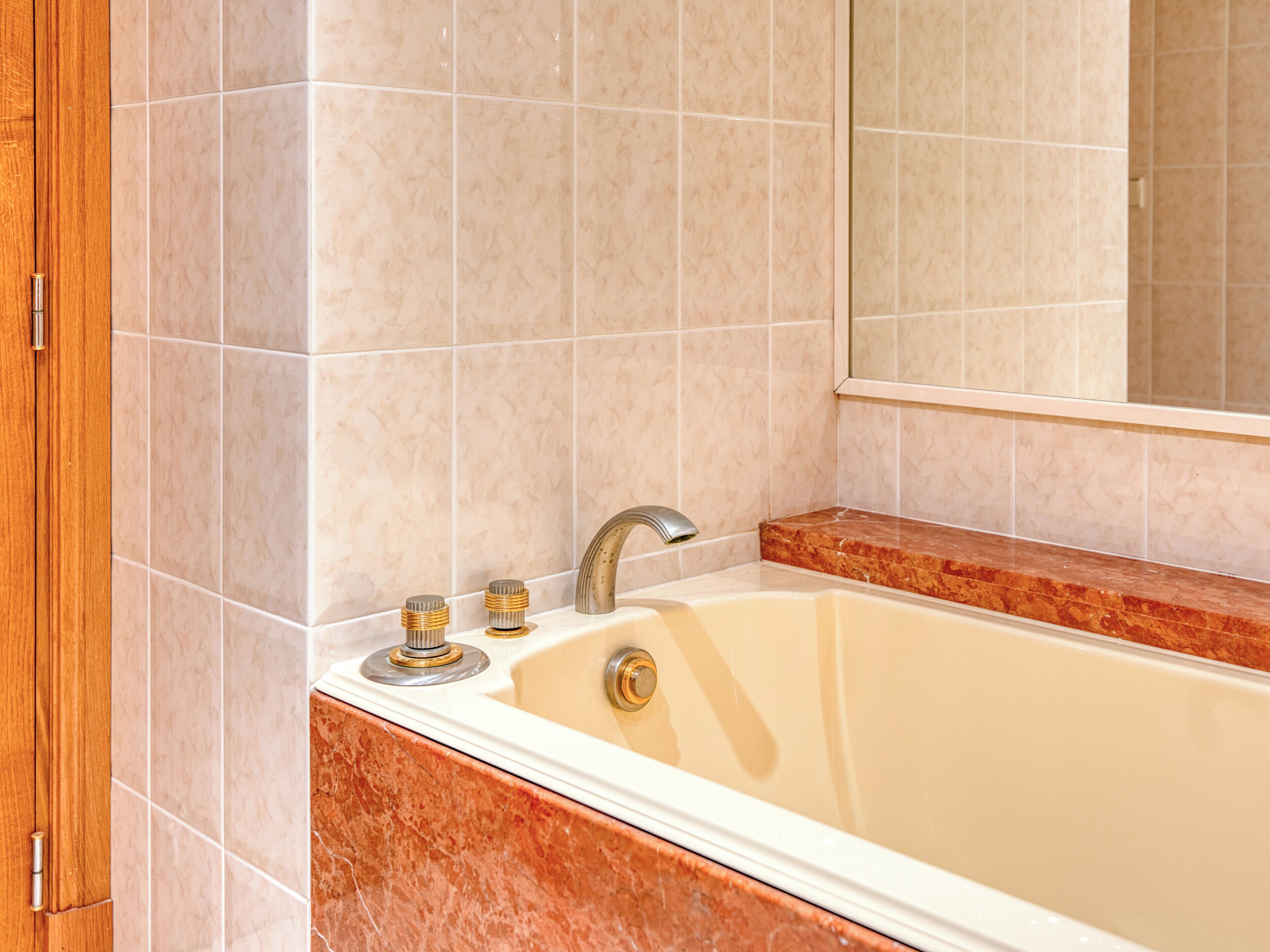 Ein Badezimmer mit einer Badewanne, einem Spiegel und einer Holztür.