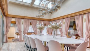 Une salle à manger spacieuse avec une longue table, des chaises roses, un vase rempli de fleurs et un lustre.