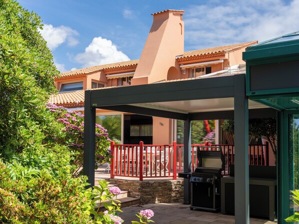 A covered patio area with a grill, a stone wall, and a red railing.