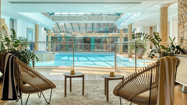 Une piscine intérieure dotée d'un toit en verre, de fauteuils en osier et offrant une vue sur l'espace piscine.