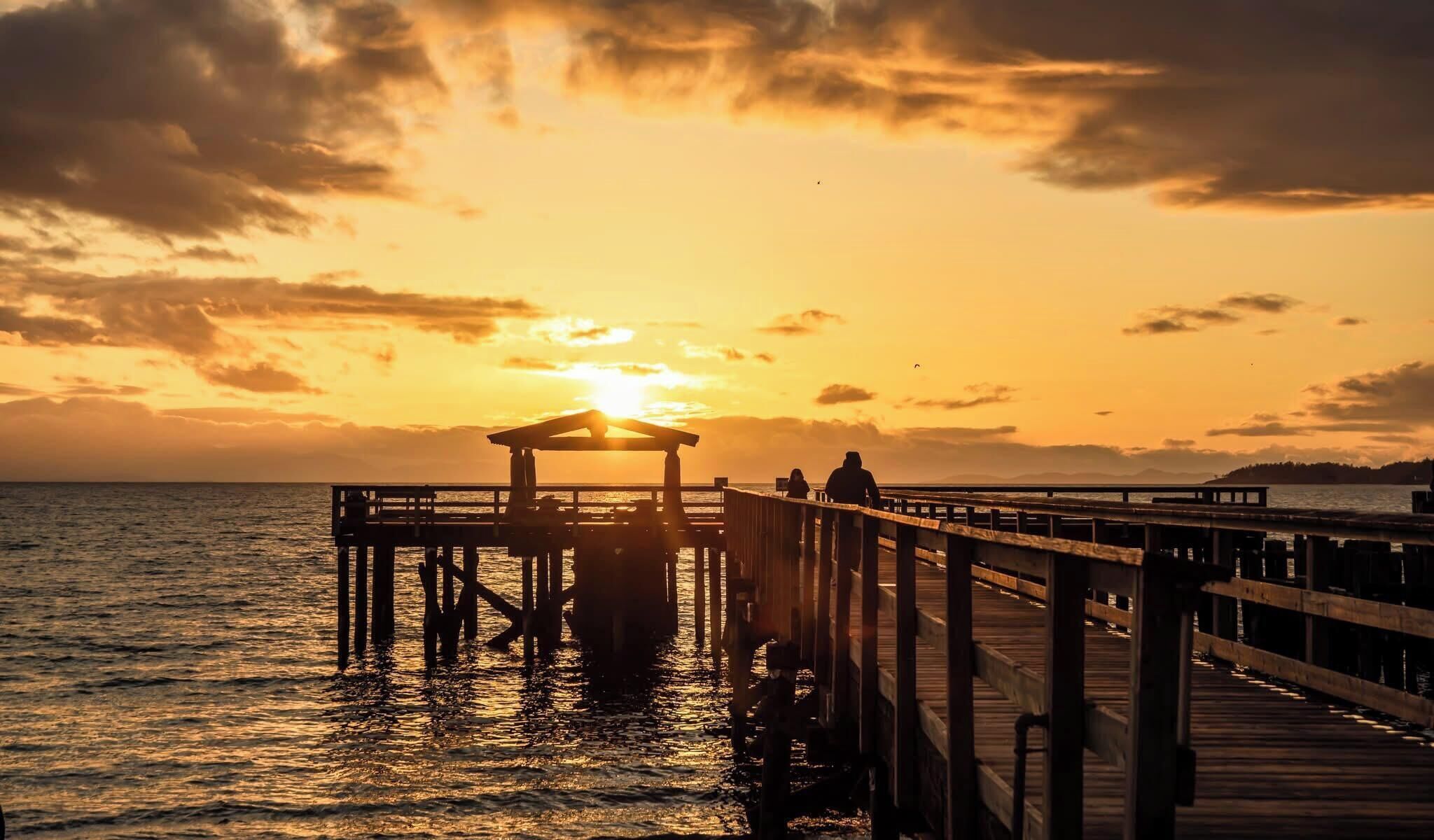 Un muelle se adentra en aguas tranquilas, con un atardecer al fondo.