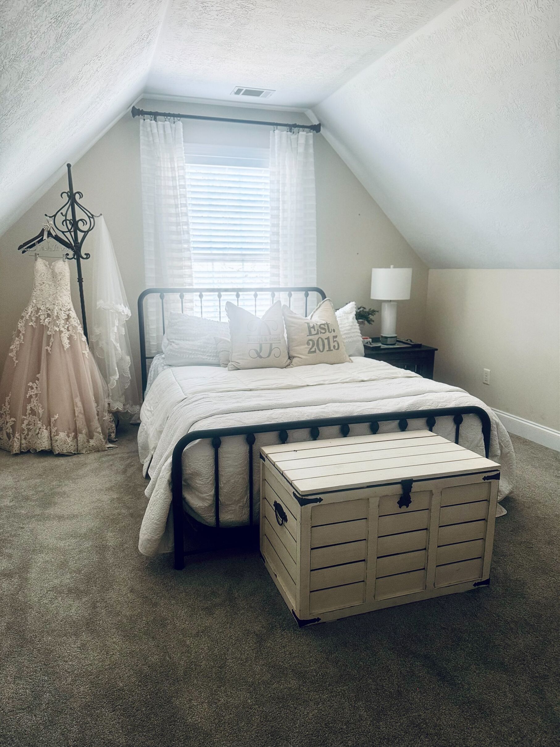 Un dormitorio con cama, mesita de noche, lámpara, cómoda y un vestido colgado.