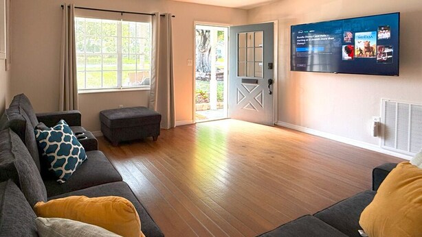 Een woonkamer met een grijze bank, voetenbankje en een flatscreentelevisie die aan de muur is bevestigd.