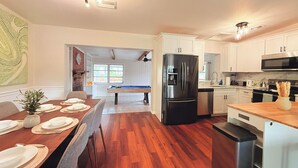 Een moderne keuken met een centraal eiland, roestvrijstalen apparatuur en een eethoek met een pooltafel.