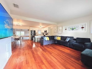A spacious living area with a dark-colored sofa set, a small kitchen, and a dining area with a table and chairs. - Ultimate Family Getaway: 4BR Home with Pool & Games (Winter Haven)