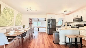 Een moderne keuken met witte kasten, een roestvrijstalen koelkast en een eethoek met een pooltafel.