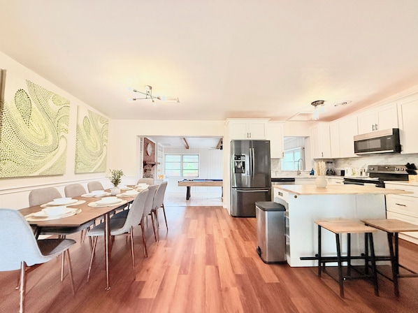 A modern kitchen with white cabinets, a stainless steel refrigerator, and a dining area with a pool table. - Ultimate Family Getaway: 4BR Home with Pool & Games (Winter Haven)
