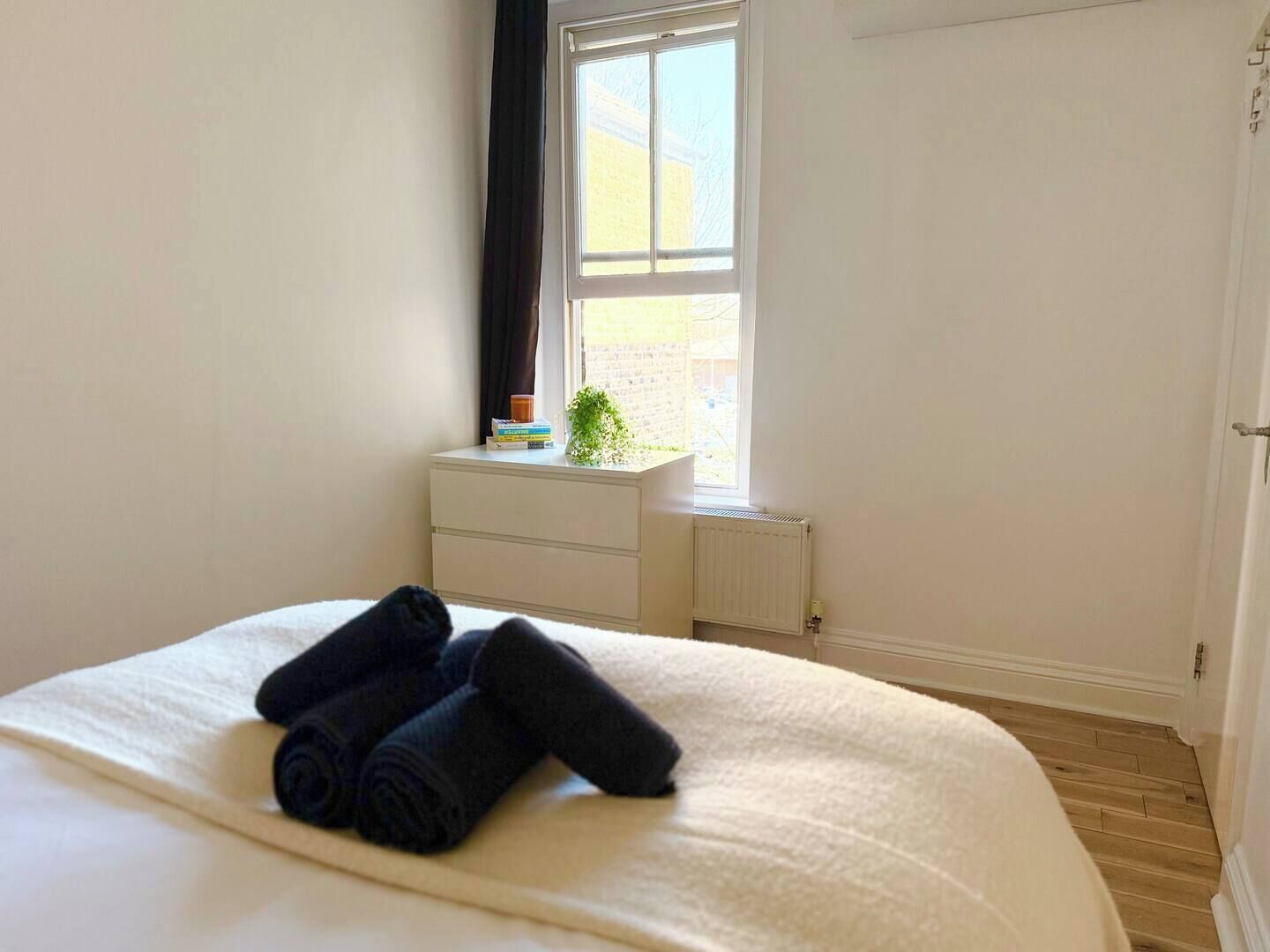A bedroom with a bed, a dresser, a radiator, a window with curtains, and a door.