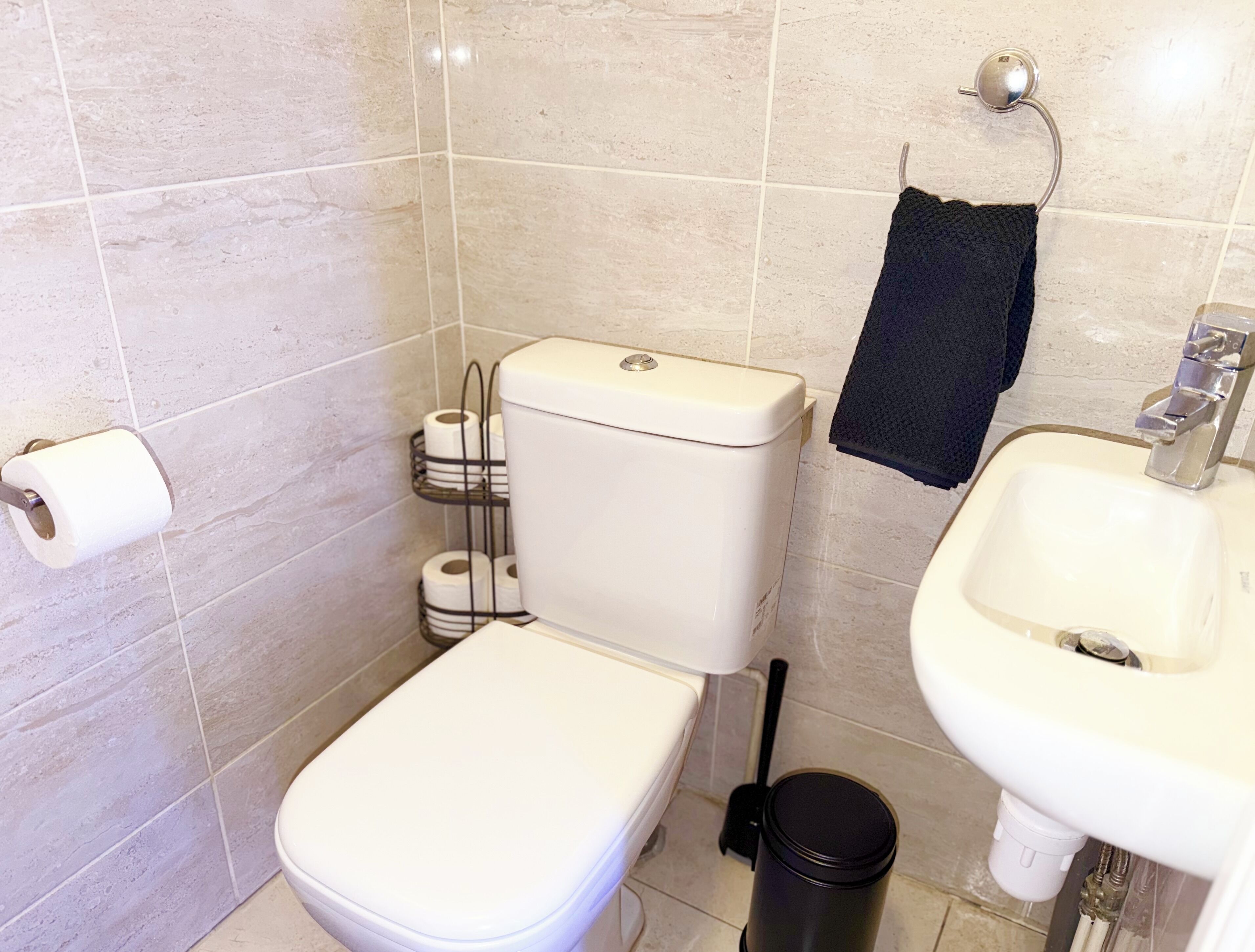 Een badkamer met een toilet, een wastafel, een handdoekhouder en een prullenbak.