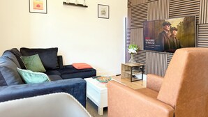 Ein Wohnzimmer mit einer Couch, einem Sessel und einem Fernseher, der eine Fernsehsendung zeigt.