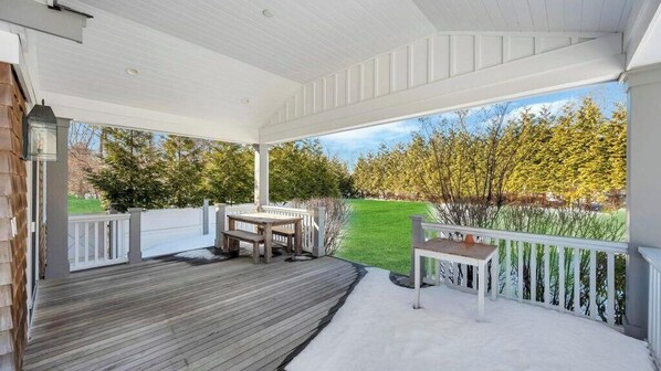 Eine überdachte Veranda mit Holzdeck, einem Tisch und einer Bank.