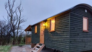 A wooden cabin with a porch, a staircase, and a wheelbarrow. - The Old Library Shepherd's Hut with Hot Tub, on the edge of the North York Moors (Pinchinthorpe)