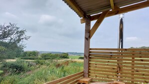 A wooden deck with a bench and a hot tub, overlooking a grassy field and trees. - The Old Library Shepherd's Hut with Hot Tub, on the edge of the North York Moors (Pinchinthorpe)