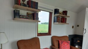 A room with two leather armchairs, a bookshelf, a window with a view of a field, and a wood-burning stove. - The Old Library Shepherd's Hut with Hot Tub, on the edge of the North York Moors (Pinchinthorpe)