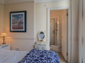 A bedroom with a bed, a bedside lamp, a dresser with a mirror, a framed picture on the wall, and a walk-in closet. - 2 St Michaels House (Lyme Regis)
