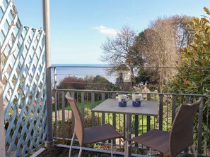 A balcony with two chairs and a table, overlooking a body of water and greenery. - 2 St Michaels House (Lyme Regis)
