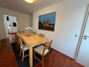 A dining area with a wooden table, chairs, a vase with flowers, and a framed picture on the wall. - Spacious 4-Room Apartment with Wi-Fi (Neustadt in Holstein)
