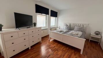A bedroom with a bed, dresser, TV, windows, and a radiator.