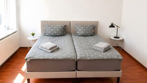 Un lit double avec une couvre-lit à motifs géométriques, deux oreillers, une table de chevet avec une lampe et une petite plante en pot.