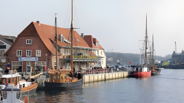 Un bâtiment situé au bord de l’eau, avec un toit rouge, une enseigne et un quai où sont amarrés des bateaux.