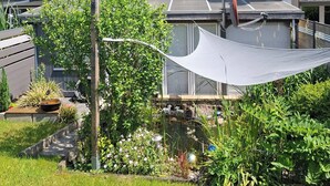 Un immeuble résidentiel doté d’un garage, d’un patio couvert et d’un jardin agrémenté de diverses plantes et d’un petit étang.