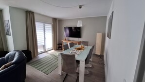 Un salon moderne comprenant un coin repas, un téléviseur à écran plat fixé au mur et une porte-fenêtre coulissante donnant sur un espace extérieur.