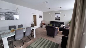 A modern living room with a sofa, armchairs, a dining table with chairs, and a coffee table.