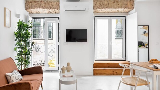 En moderne stue med sofa, spisebord, fjernsyn og et stort vindue med udsigt til gaden.