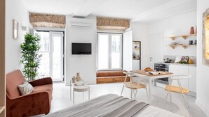 En moderne lejlighed med seng, skrivebord, stol, sofa, fjernsyn og et køkkenområde.