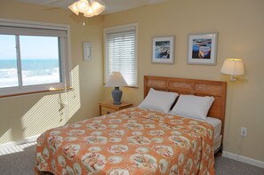 A bedroom with a bed, a nightstand, a lamp, a window with blinds, and two framed pictures on the wall. - Southern Aire - a spacious 5-bedroom oceanfront in Surf City, NC (Surf City)