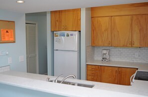A kitchen with wooden cabinets, a white refrigerator, a coffee maker, and a sink. - Southern Aire - a spacious 5-bedroom oceanfront in Surf City, NC (Surf City)