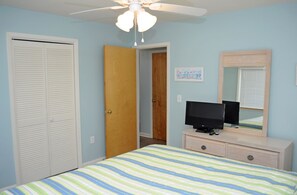 A bedroom with a bed, a television on a dresser, a ceiling fan, and a door leading to another room. - Southern Aire - a spacious 5-bedroom oceanfront in Surf City, NC (Surf City)