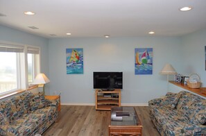 A living room with two patterned sofas, a flat-screen TV, and artwork depicting sailboats. - Southern Aire - a spacious 5-bedroom oceanfront in Surf City, NC (Surf City)