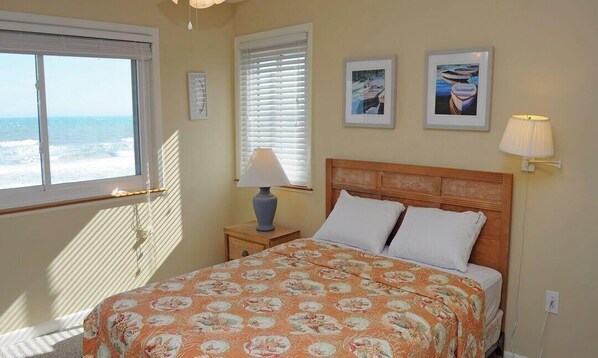 A bedroom with a bed, a window with blinds, a lamp, and two framed pictures on the wall. - Southern Aire - a spacious 5-bedroom oceanfront in Surf City, NC (Surf City)