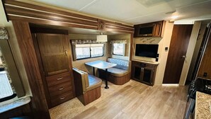 Interior compacto de una autocaravana con kitchenette, comedor y un pequeño rincón de estar.