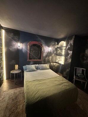 A bedroom with a bed, a round side table, a chair, and wall sconces. - Hostal Mustelier (Barcelona)