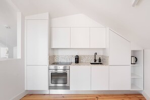 Una cocina moderna con armarios blancos, horno de acero inoxidable, cafetera y hervidor.