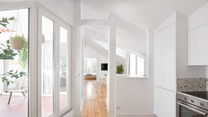 A modern kitchen with white cabinets, a wooden floor, and a view into the living area. - Spacious 6-Bedroom Apt w/ Sunny Terrace in Lisbon (Lisbon)