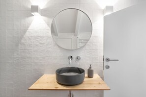 Un baño con un espejo redondo, un tocador de madera, un lavabo y una puerta.