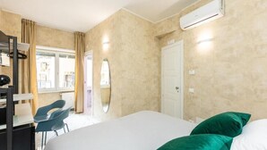 A hotel room with a bed, a desk, a chair, an air conditioning unit, and a door. - Flowery Rainbow (Rome)