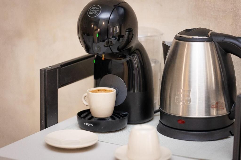 A coffee machine, a cup of coffee, a kettle, and a plate on a table.