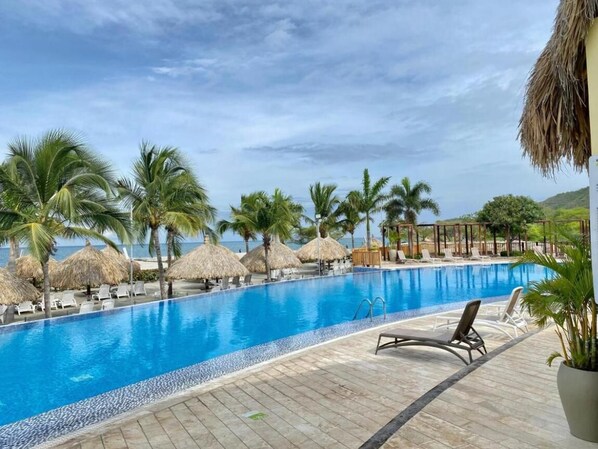 Une piscine bordée de chaises longues, de palmiers et offrant une vue sur l’océan.