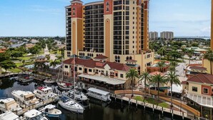 A high-rise hotel with multiple balconies, a marina with boats, and a marina with a covered walkway. - Cape Harbour Luxury Condo, 2 King Beds, Pool, Shops & Restaurants (Cape Coral)