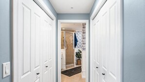 A hallway with white doors, a shower area, and a plant. - Cape Harbour Luxury Condo, 2 King Beds, Pool, Shops & Restaurants (Cape Coral)