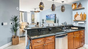 A modern kitchen with granite countertops, wooden cabinets, a built-in dishwasher, and pendant lighting. - Cape Harbour Luxury Condo, 2 King Beds, Pool, Shops & Restaurants (Cape Coral)