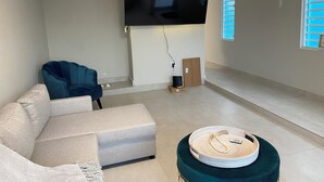 Ein Wohnzimmer mit flachbildfernseher an der Wand, einem Sofa, einem Couchtisch und einer Klimaanlage.