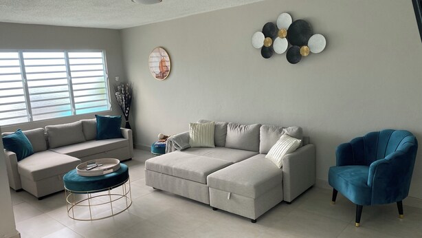 Ein Wohnzimmer mit einem Ecksofa, einem blauen Sessel, einem Couchtisch und einer Wanddekoration.