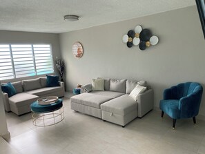 Ein Wohnzimmer mit einem Ecksofa, einem blauen Sessel, einem Couchtisch und einer Wanddekoration.