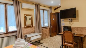 Habitación de hotel con cama, escritorio, silla, televisor y ventana con cortinas.
